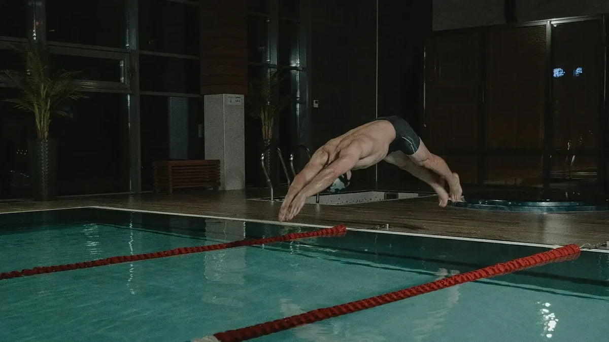 Male swimmer diving into an indoor lap pool between red lane ropes