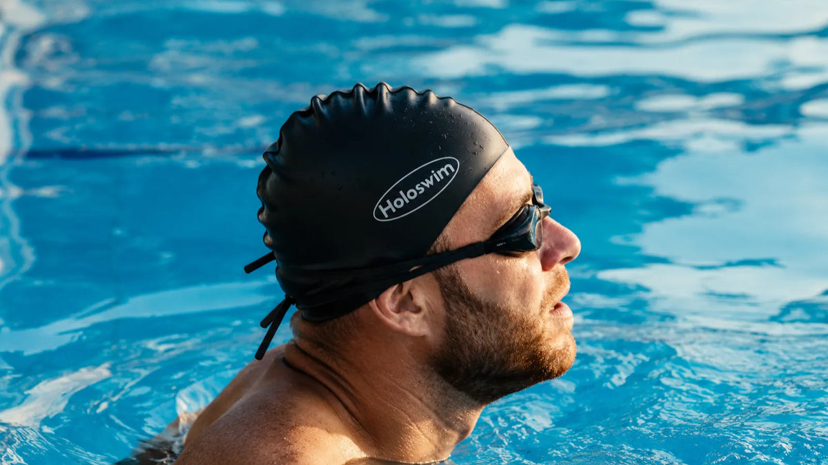 Swimmer wearing goggles and a swim cap in a blue swimming pool during training.