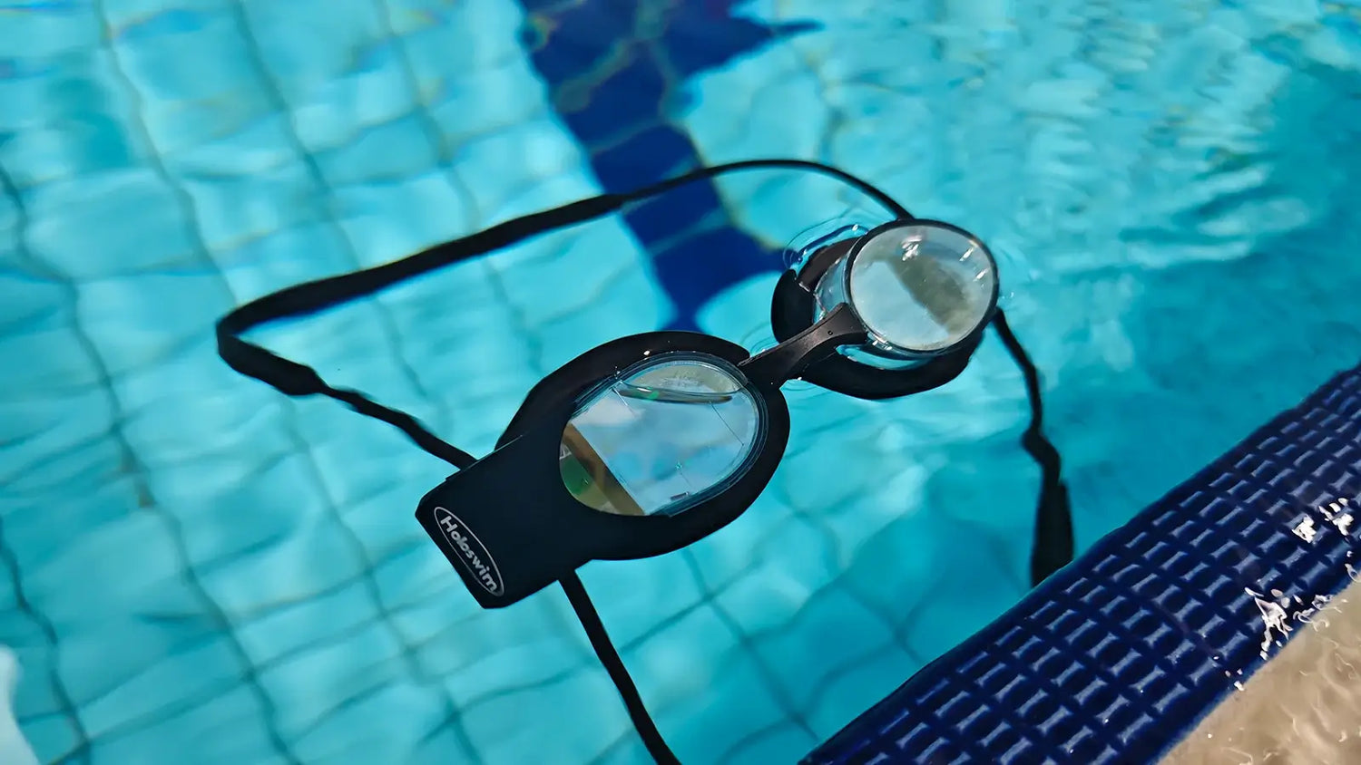HoloSwim smart swimming goggles resting in a pool with clear lenses