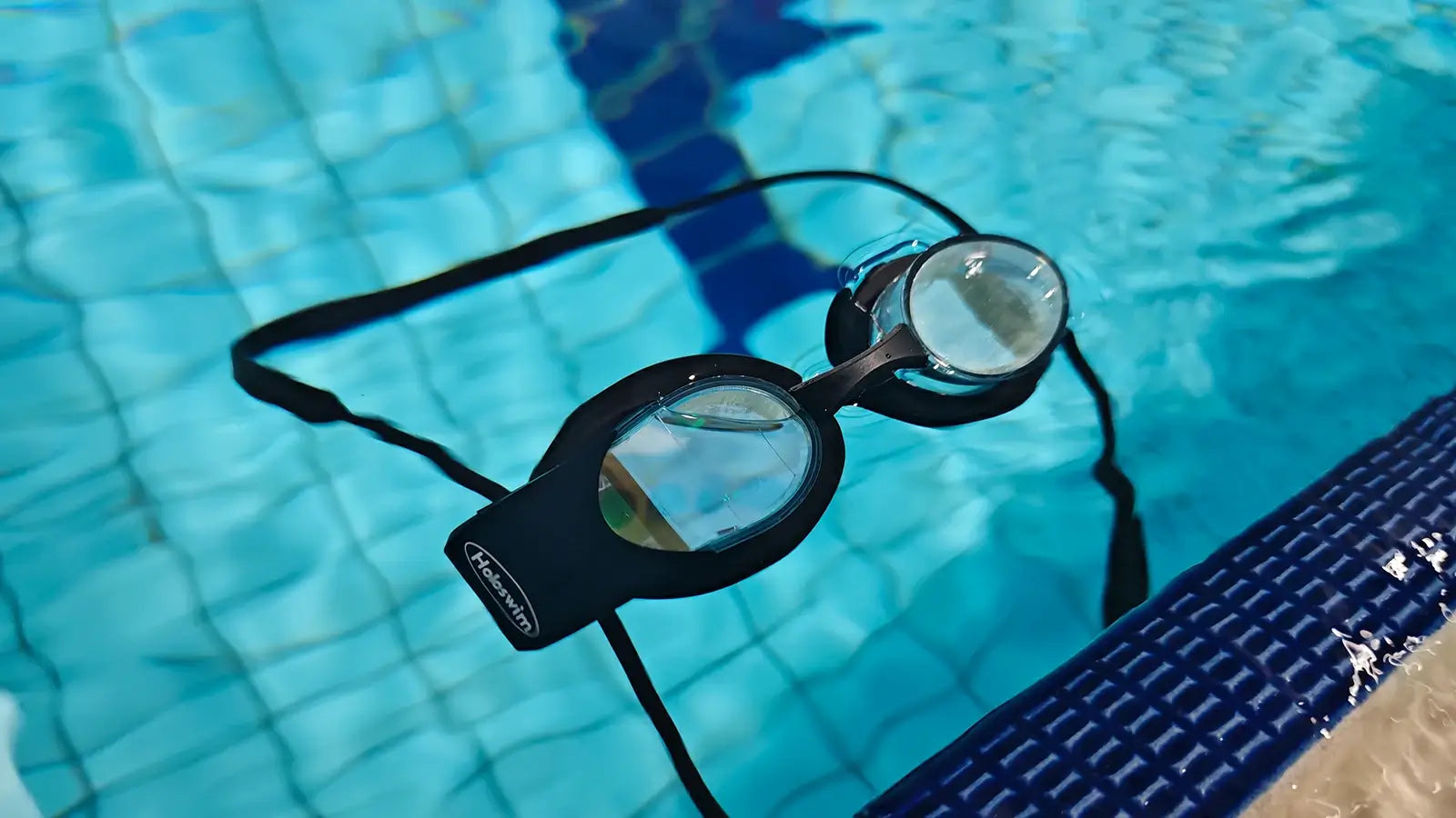 HoloSwim smart swimming goggles resting in a pool with clear lenses