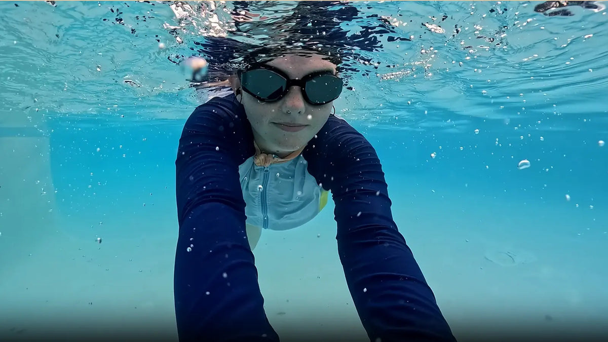 Elizabeth swimming underwater with SollaWave music goggles in a pool