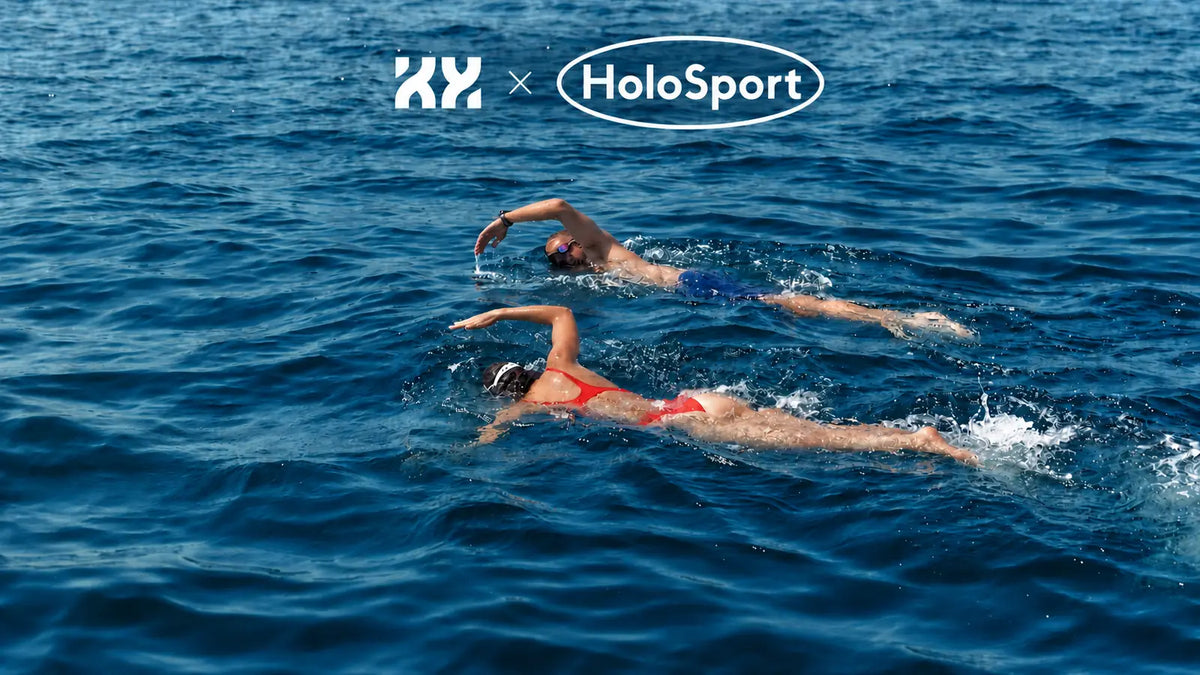 Two swimmers racing in open water at KYMA Marseille beneath KYMA and HoloSport logos