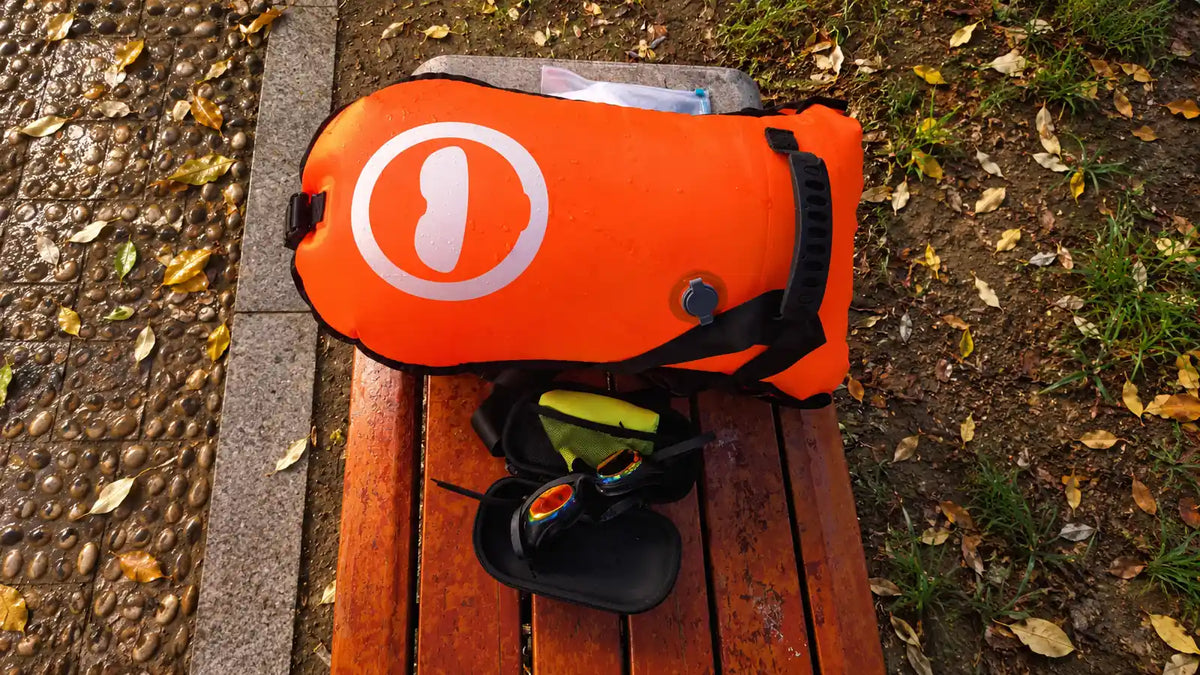 Orange open-water swim bag with goggles and a protective case on a wet bench