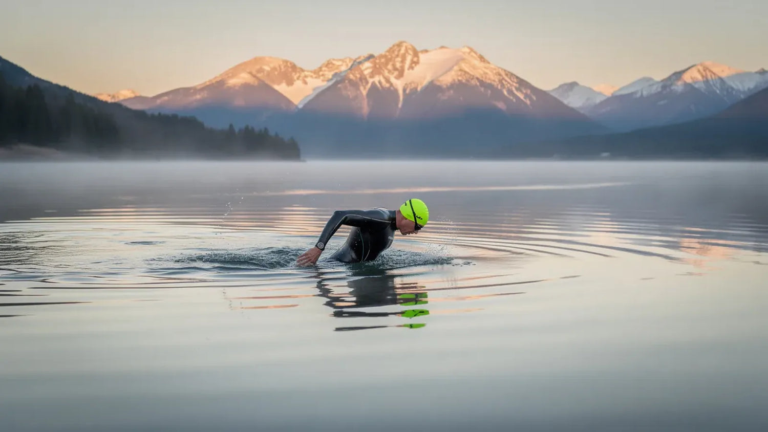 Open-water swimmer in a wetsuit and bright cap crossing a calm mountain lake