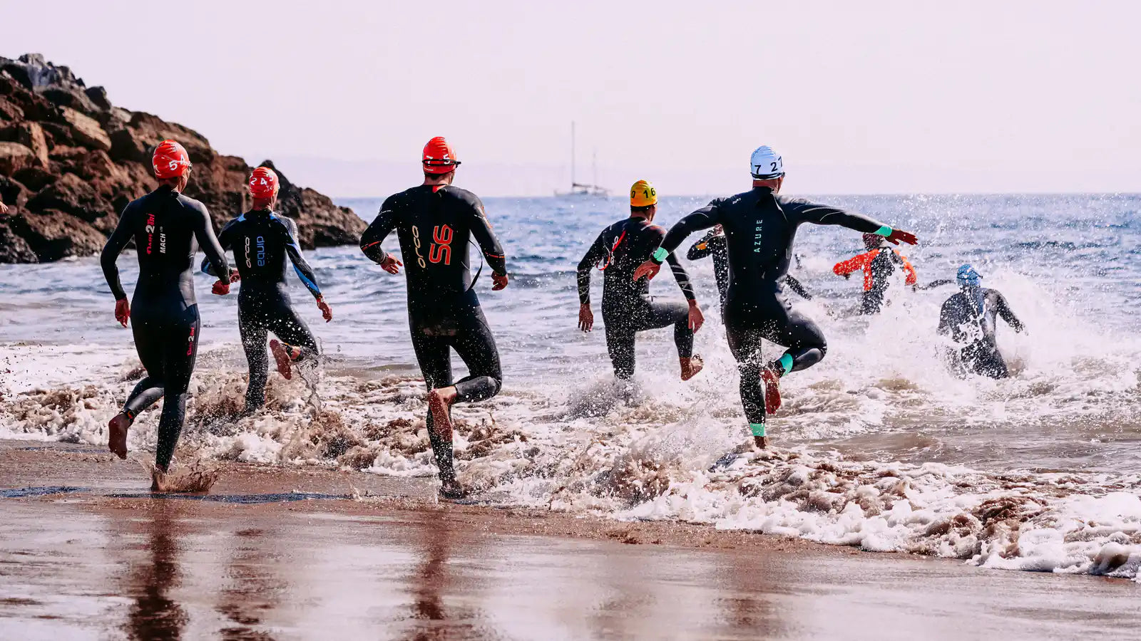 Triathletes in wetsuits entering the ocean for the swim start